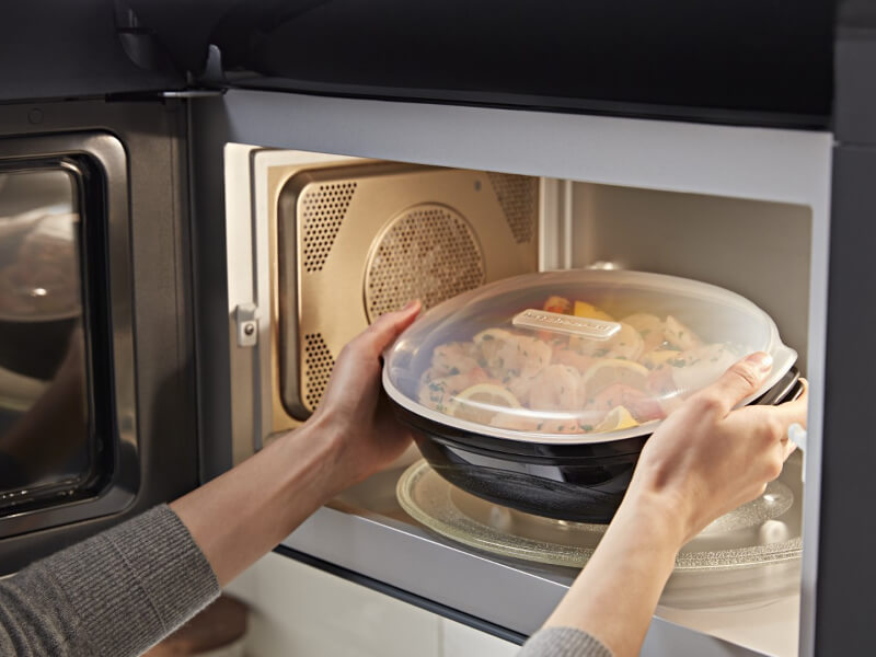 Person microwaving veggies in a microwave-safe container