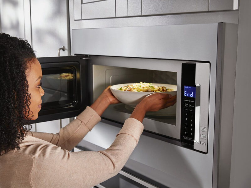 Person taking a bowl of pasta out of a built-in microwave Person taking a bowl of pasta out of a built-in microwave