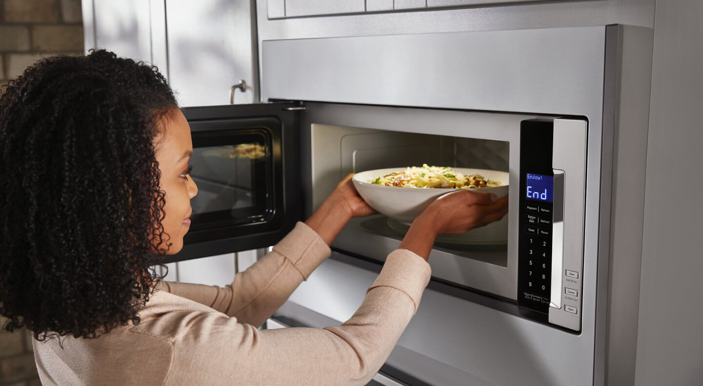 Person taking a bowl of pasta out of a built-in microwave Person taking a bowl of pasta out of a built-in microwave