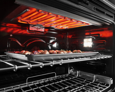 The inside of an oven range with the top burner hearing and a tray on the top rack