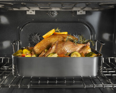 A turkey in a roasting pan on the top rack inside an oven range