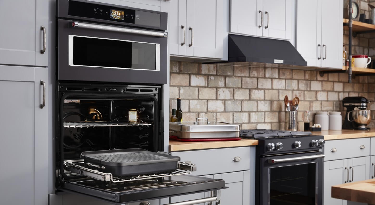 Grey kitchen cabinets, a black KitchenAid brand combination microwave wall oven and a black KitchenAid brand oven range