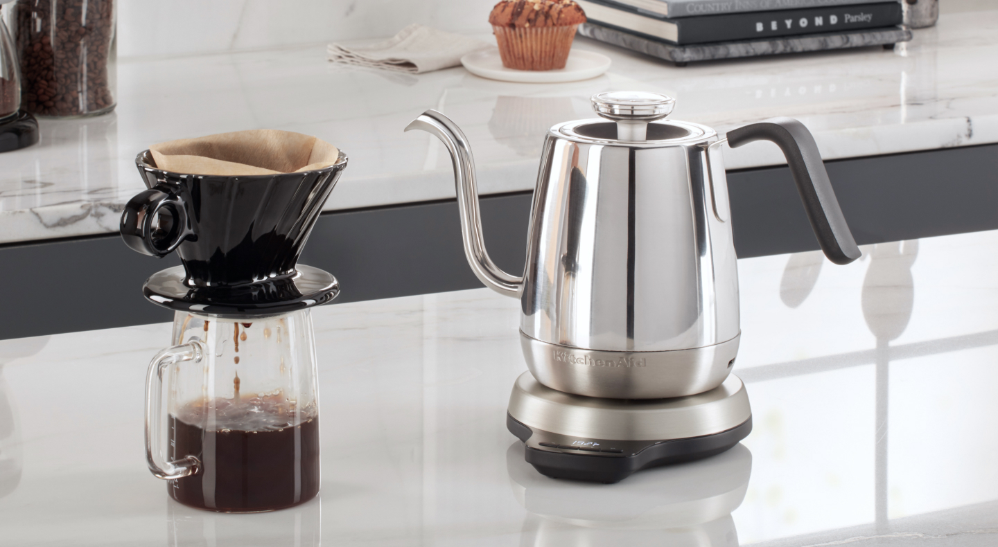 Silver KitchenAid® gooseneck kettle on white countertop with cup of pour over coffee Silver KitchenAid® gooseneck kettle on white countertop with cup of pour over coffee