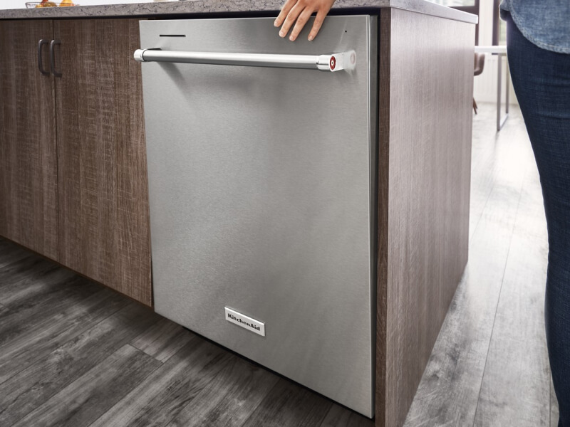 A hand closing a stainless steel dishwasher