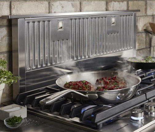 Filets cooking in a pan on a cooktop with a downdraft range hood behind it