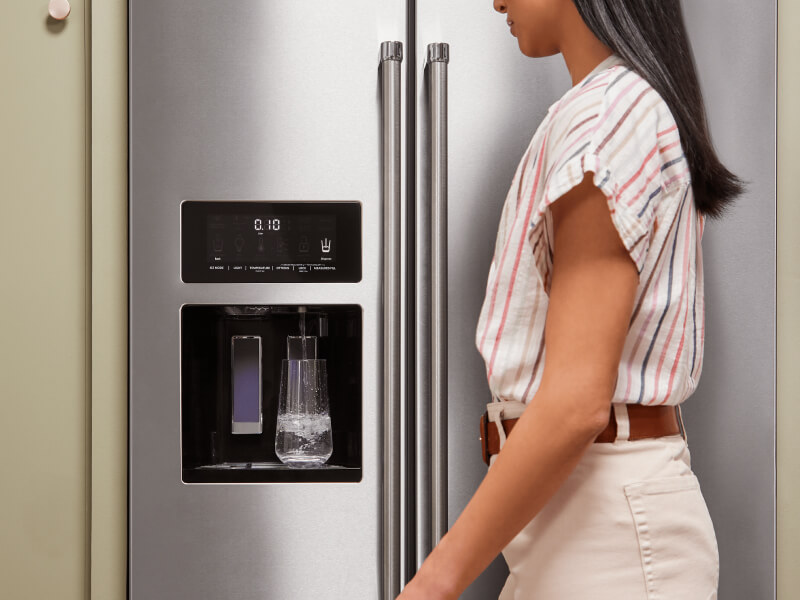 A person filling a glass of water using their refrigerator’s interior water dispenser A person filling a glass of water using their refrigerator’s interior water dispenser