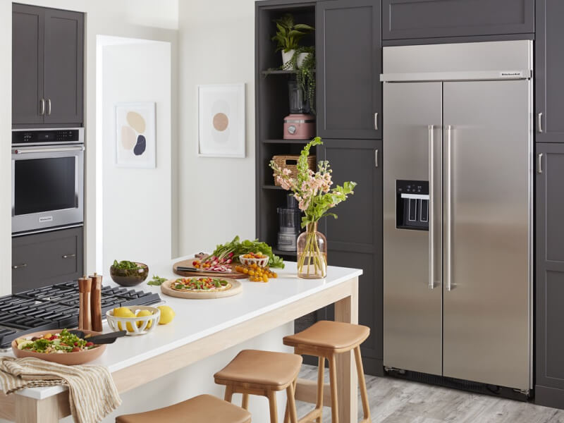 A kitchen with an island and a stainless steel side-by-side refrigerator A kitchen with an island and a stainless steel side-by-side refrigerator