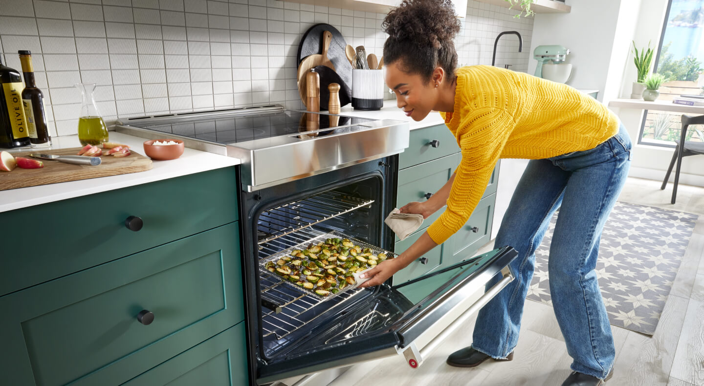 Person removing a tray of roasted vegetables from a slide-in range oven