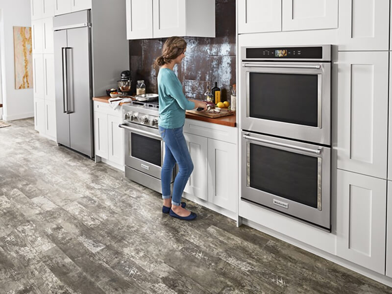 A person standing at a counter next to a wall oven preparing food