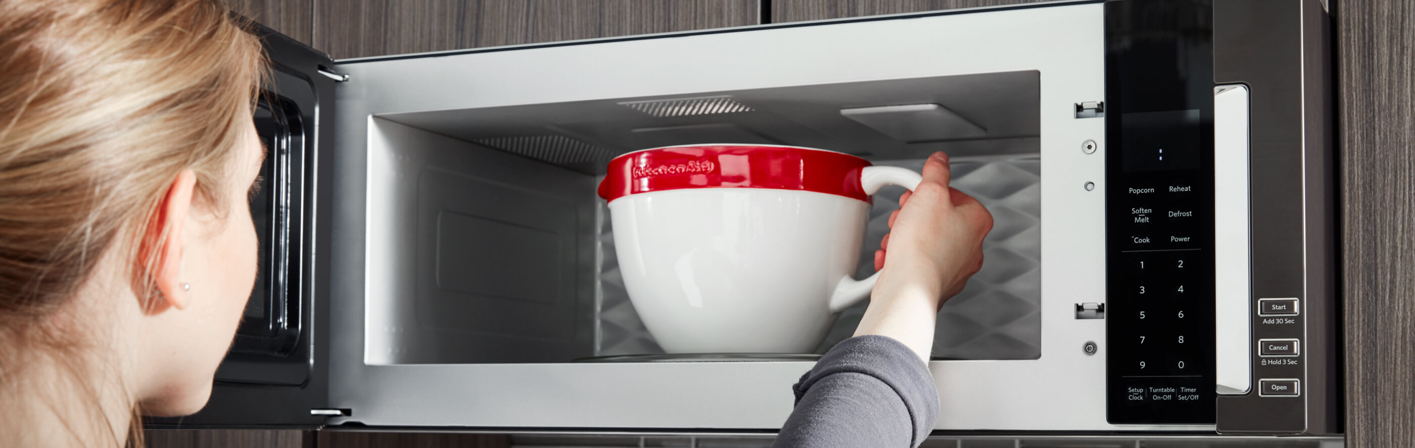 A person placing a bowl in a KitchenAid® microwave