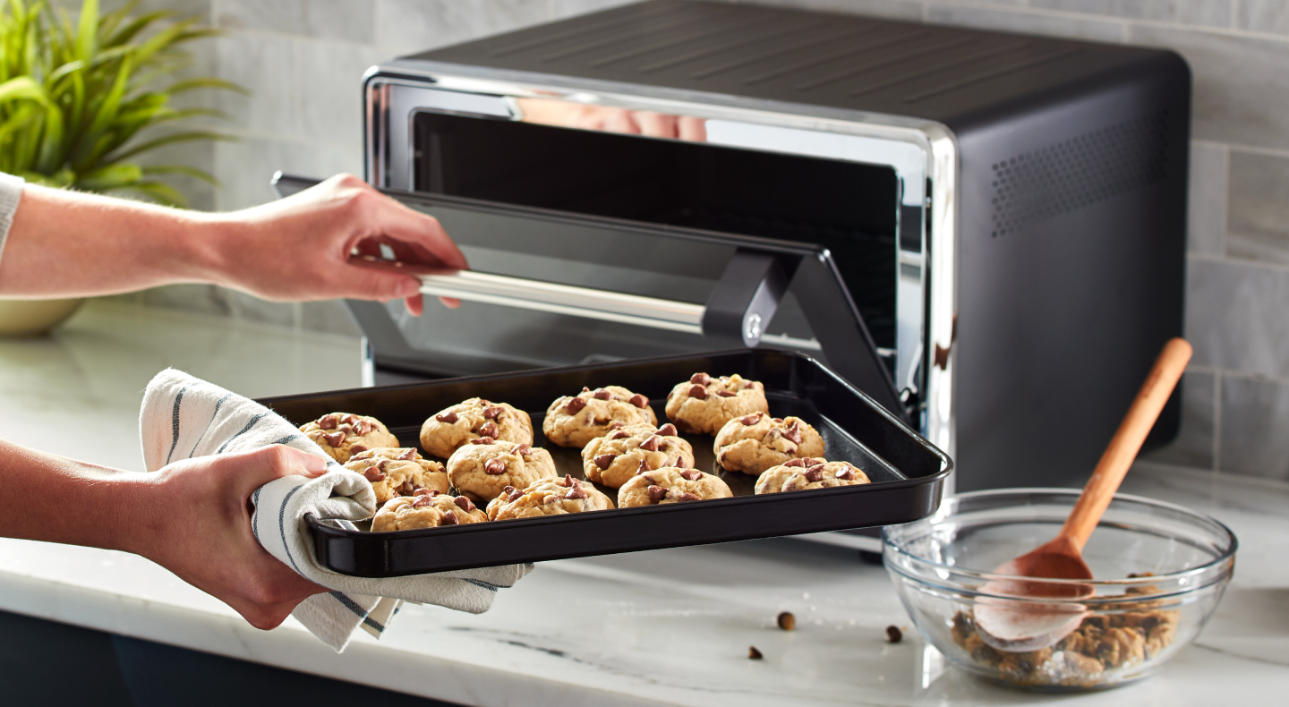Person placing a tray of cookies into a KitchenAid® countertop oven Person placing a tray of cookies into a KitchenAid® countertop oven