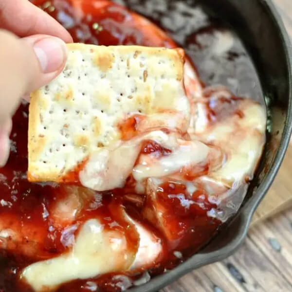 Cracker dipping into baked brie