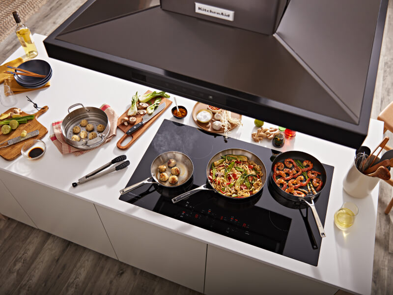 Overhead view of KitchenAid® range hood and pans with food on black cooktop