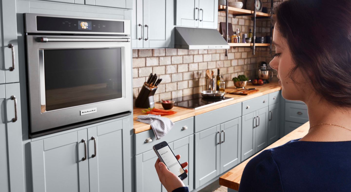 A woman checking a smartphone to control a smart oven A woman checking a smartphone to control a smart oven
