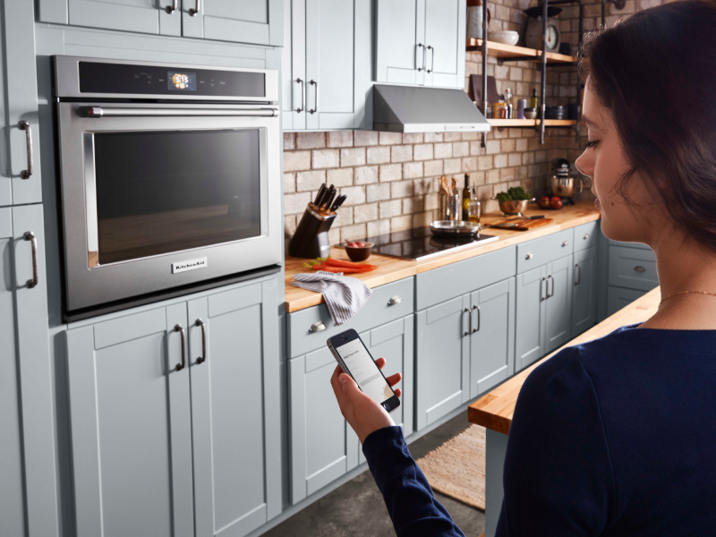 A woman checking a smartphone to control a smart oven A woman checking a smartphone to control a smart oven