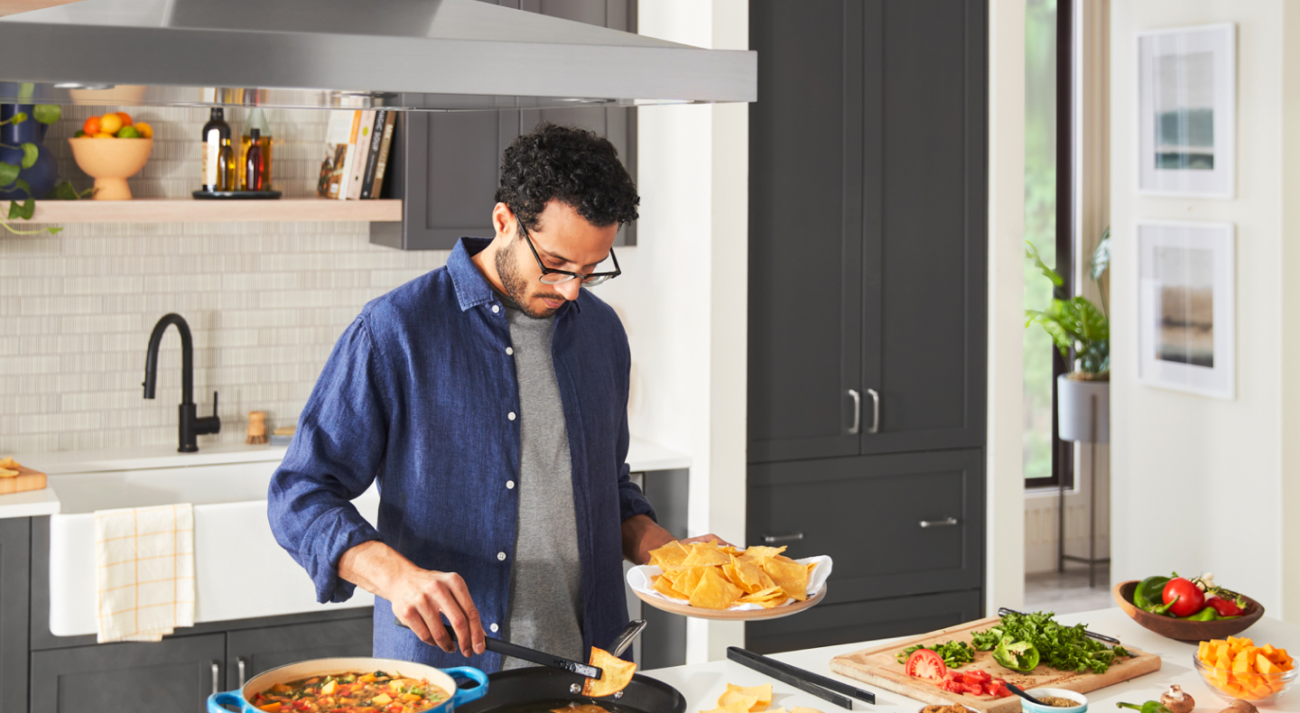 Man cooking in a kitchen with a black panel-ready french door refrigerator Man cooking in a kitchen with a black panel-ready french door refrigerator