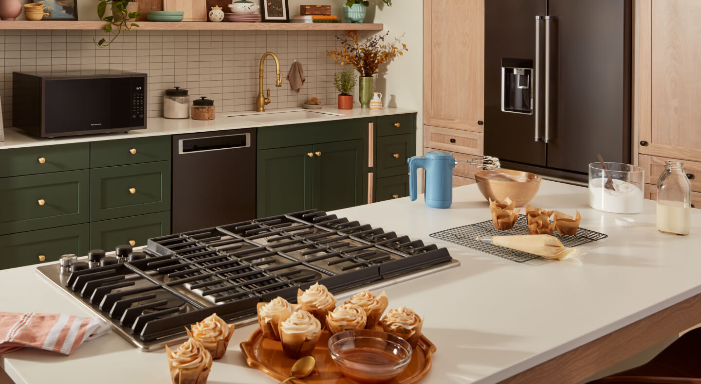 A downdraft gas range set into the island of a kitchen with green cabinetry