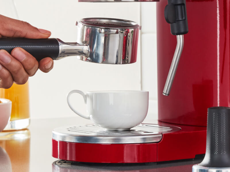Person holding espresso machine portafilter above teacup