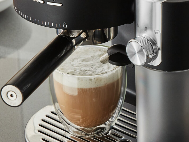 Cappuccino with foam resting on cup holder of espresso machine