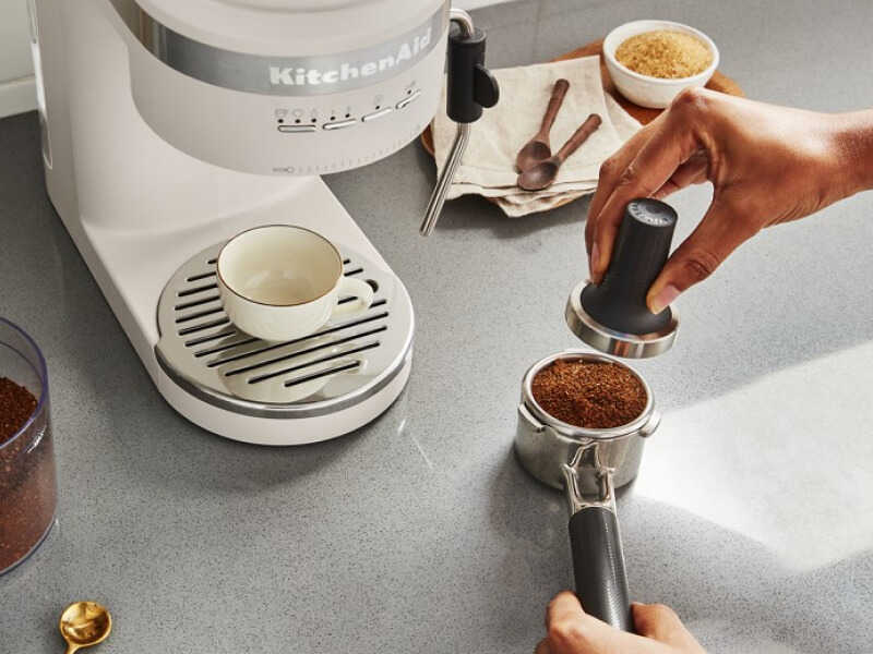 Person tamping down coffee grounds in portafilter of espresso machine