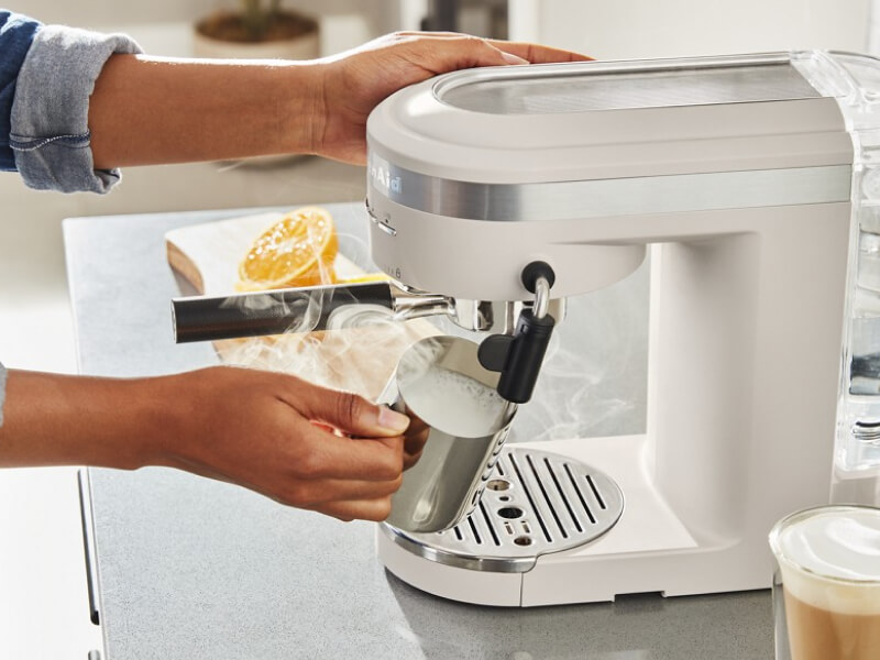 Person steaming milk in pitcher using a white espresso machine