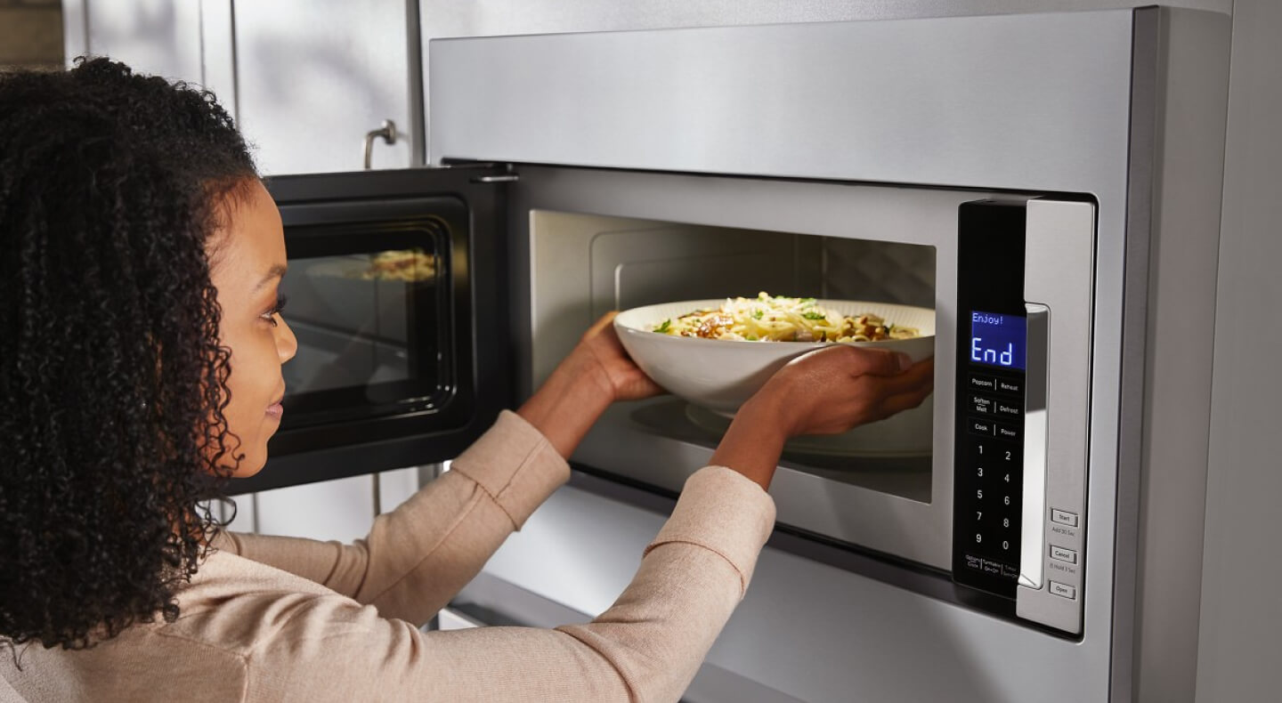 A woman putting food into a microwave
