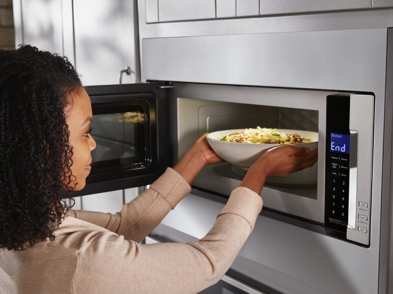 A woman putting food into a microwave