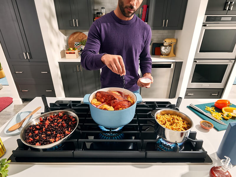 A person sprinkling seasonings over a meal simmering in a Dutch oven