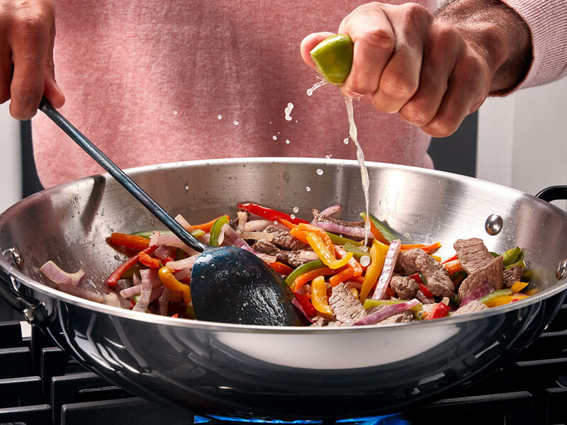 Someone squeezing lime juice over veggies in a pan