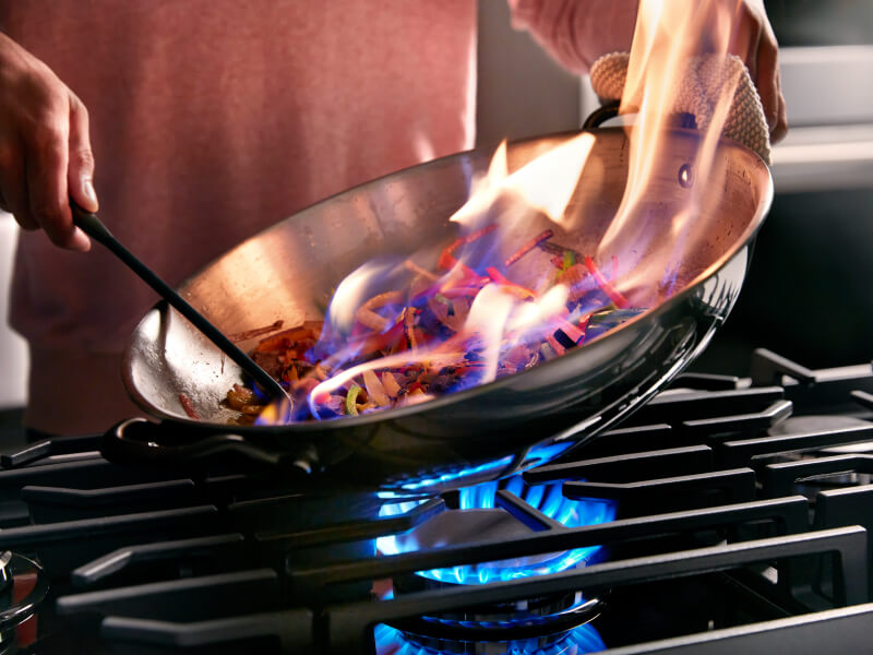 Person using a stick lighter to light alcohol fumes in a skillet