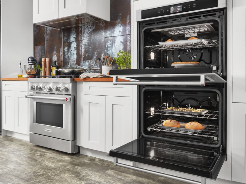 An opened KitchenAid® double oven next to a gas range An opened KitchenAid® double oven next to a gas range