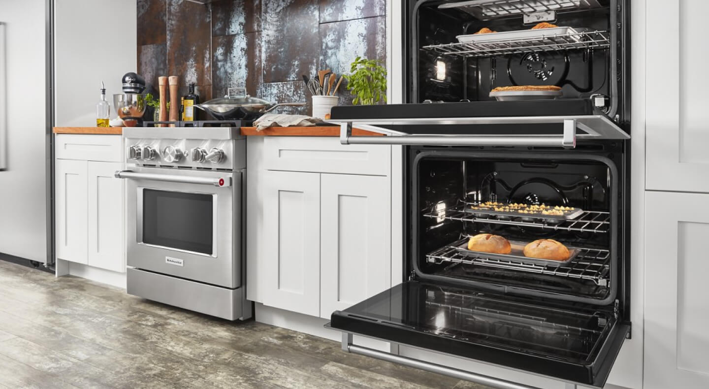 An opened KitchenAid® double oven next to a gas range An opened KitchenAid® double oven next to a gas range