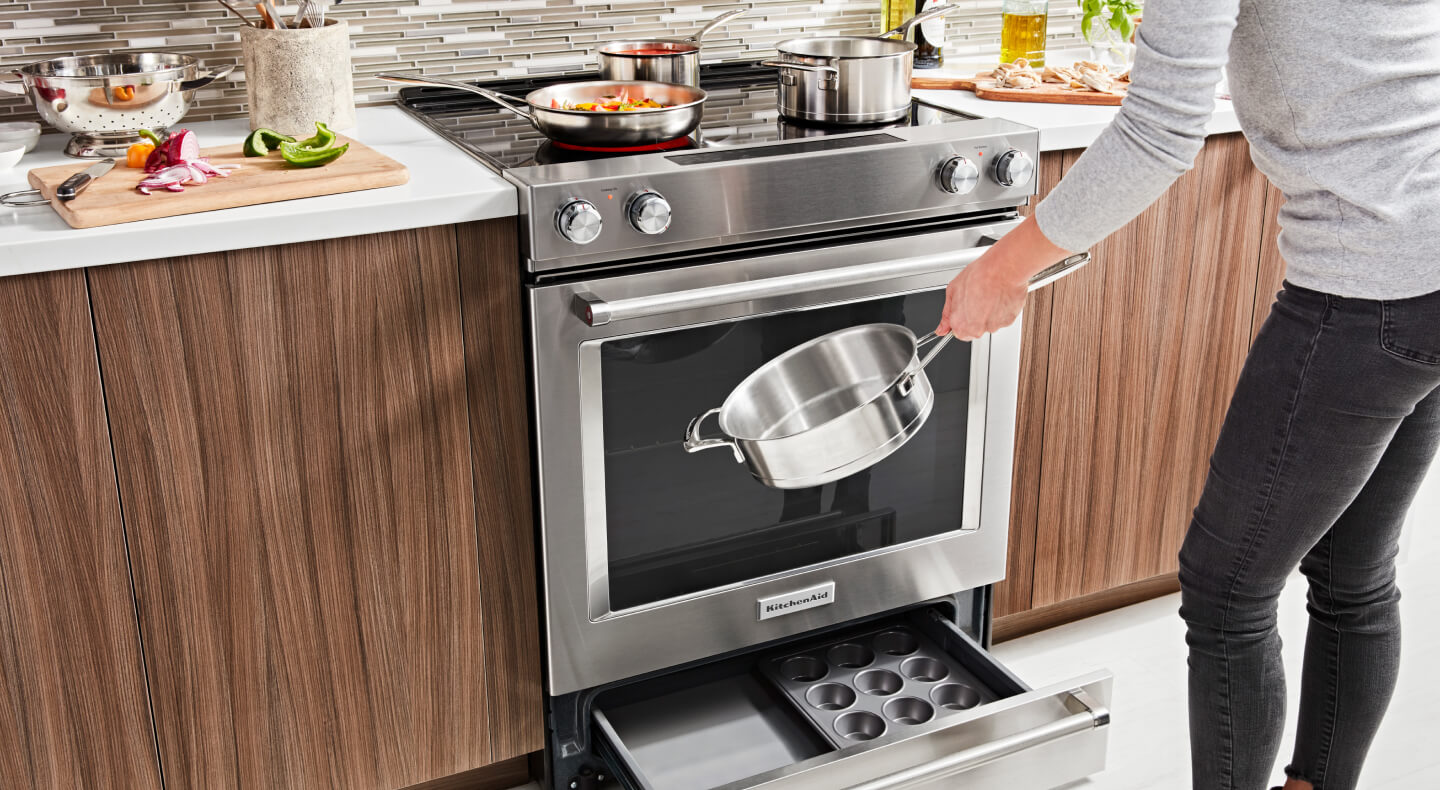 A slide-in range with an open storage drawer showing pans inside