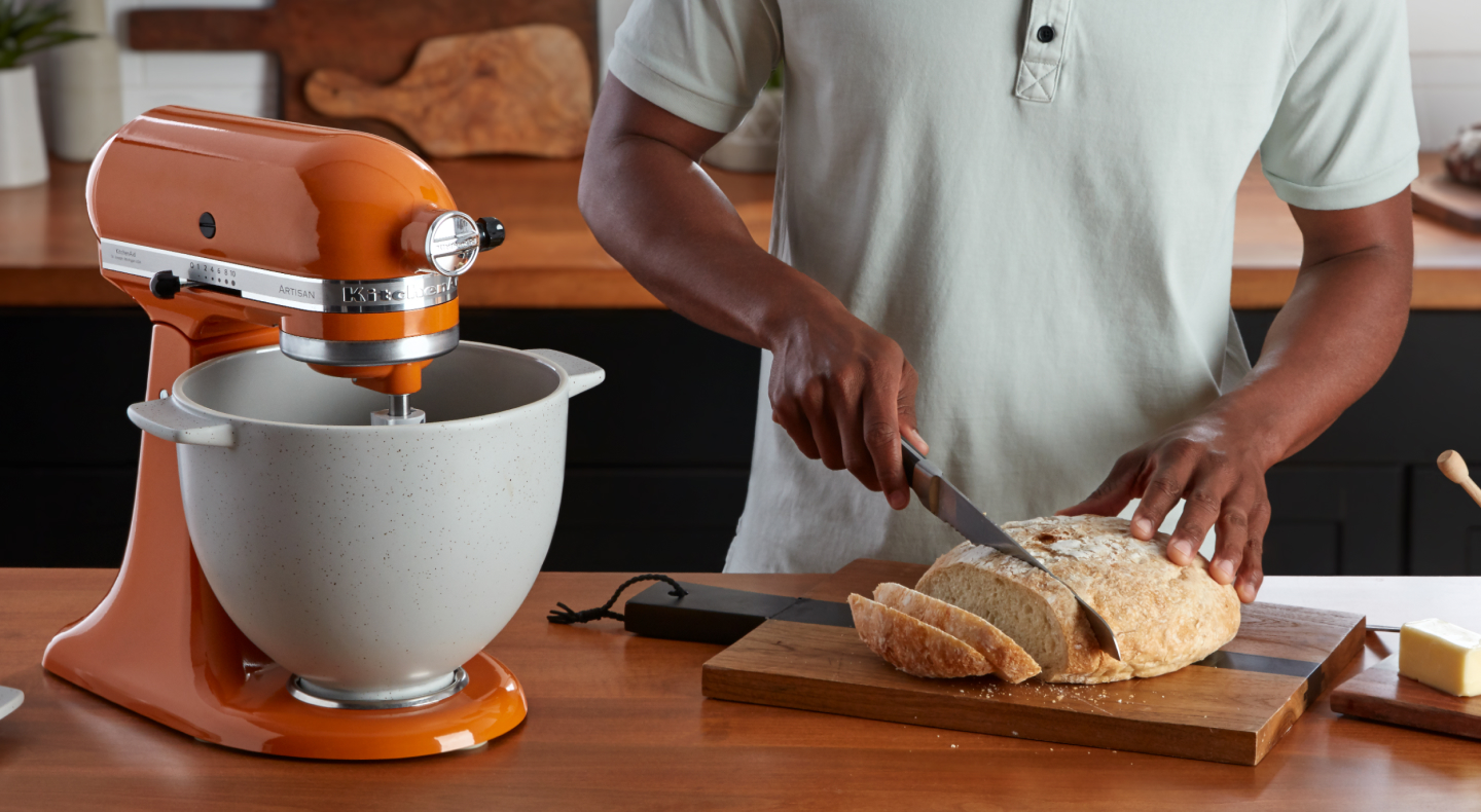 A person slicing bread next to an orange KitchenAid® stand mixer A person slicing bread next to an orange KitchenAid® stand mixer