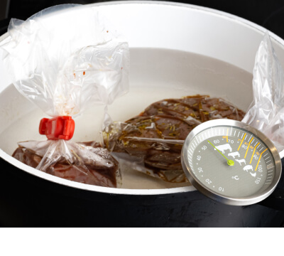 Two pieces of meat in sous vide bags placed inside a pot with a thermometer