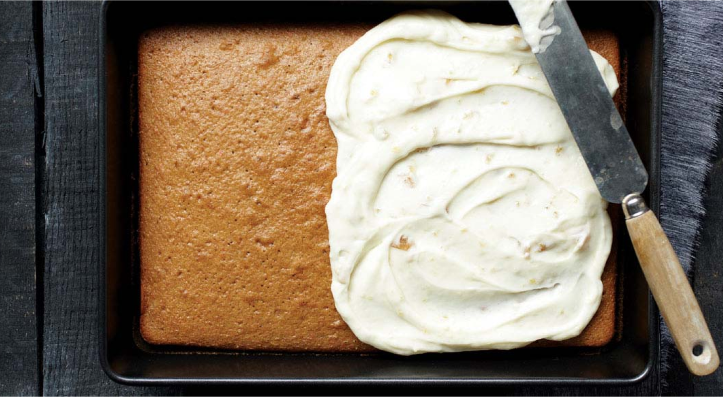 A half frosted white cake in a rectangle baking pan. 