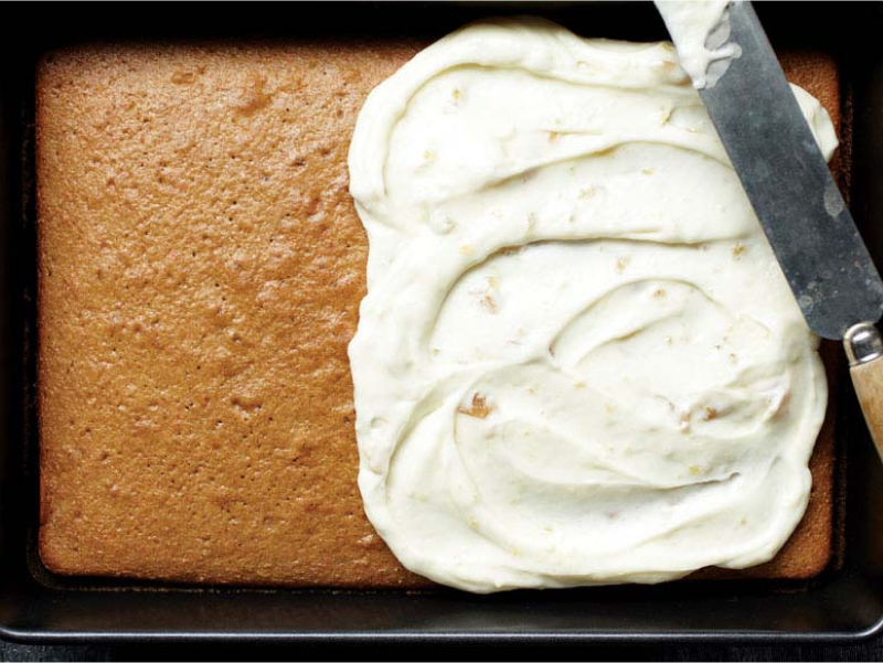 A half frosted white cake in a rectangle baking pan.