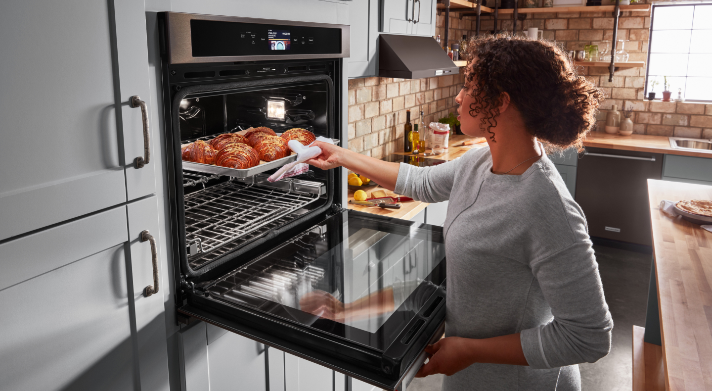 Person removing pastries from a KitchenAid® single wall oven in light gray cabinetry