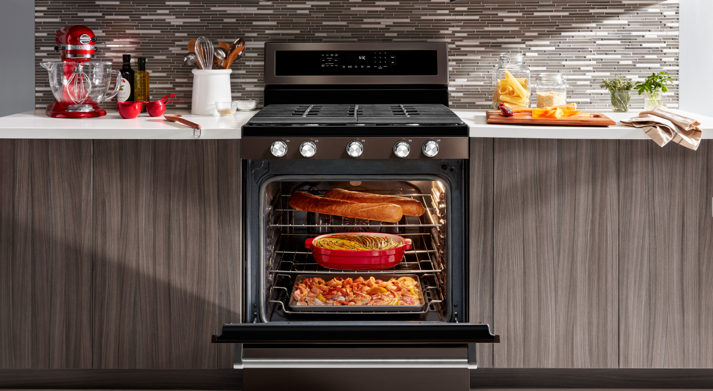 An open gas stove door filled with dishes cooking An open gas stove door filled with dishes cooking