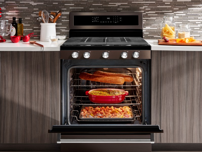 An open gas stove door filled with dishes cooking An open gas stove door filled with dishes cooking