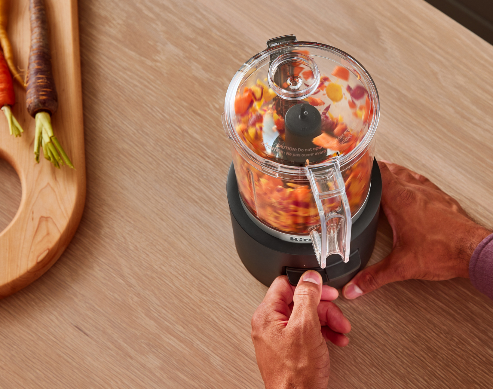 A person using the KitchenAid Go™ Cordless Food Chopper to chop orange, purple and yellow vegetables.