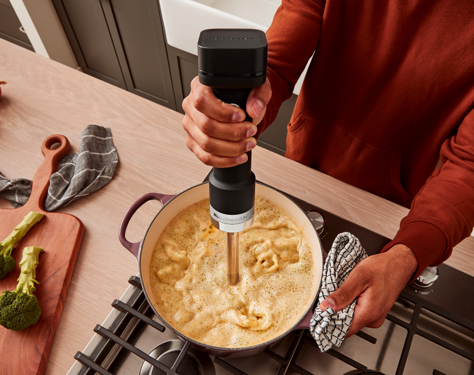 A person using the KitchenAid Go™ Cordless Hand Blender to blend soup.