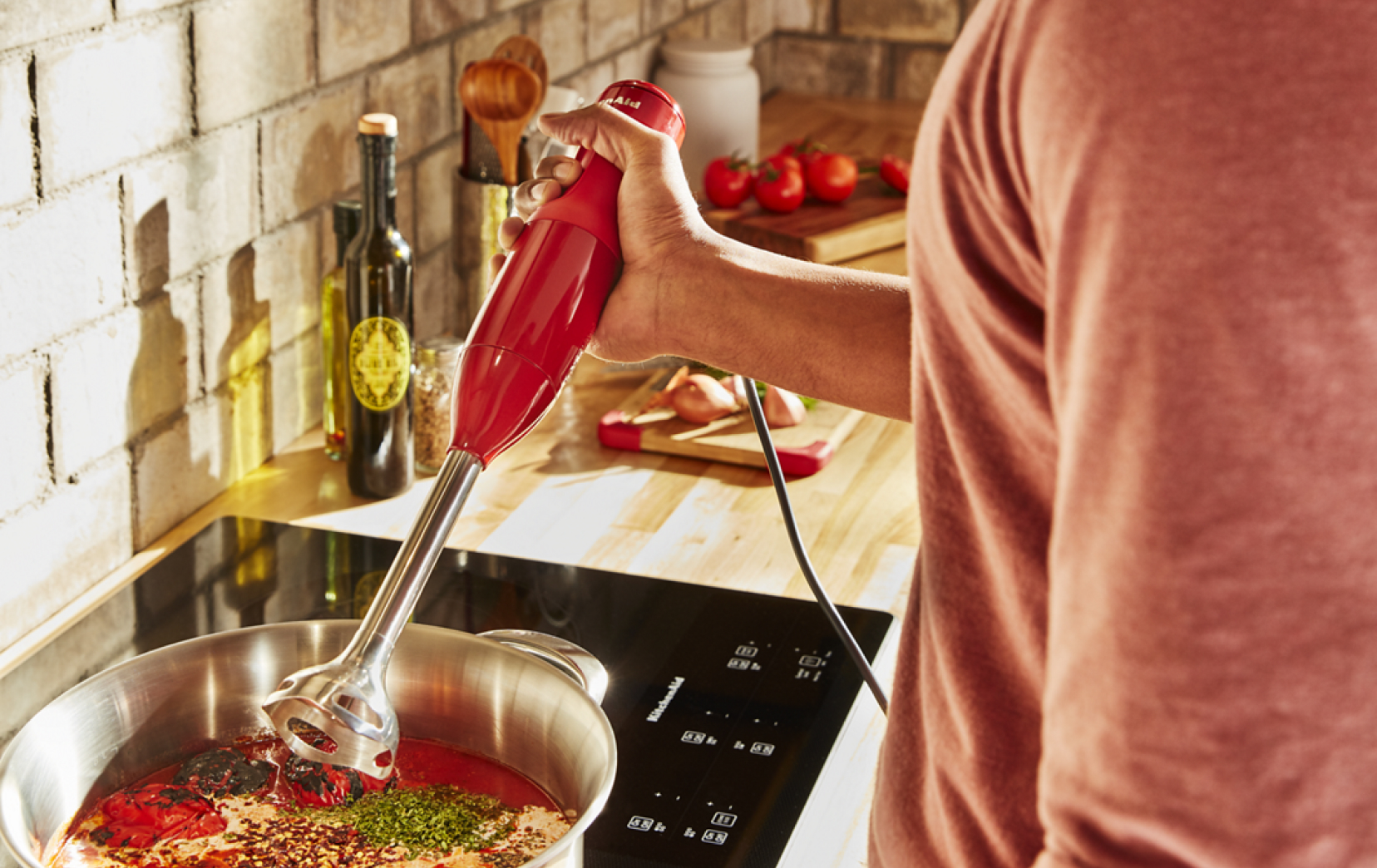 A person using a 2-Speed Hand Blender to blend sauce on a cooktop.