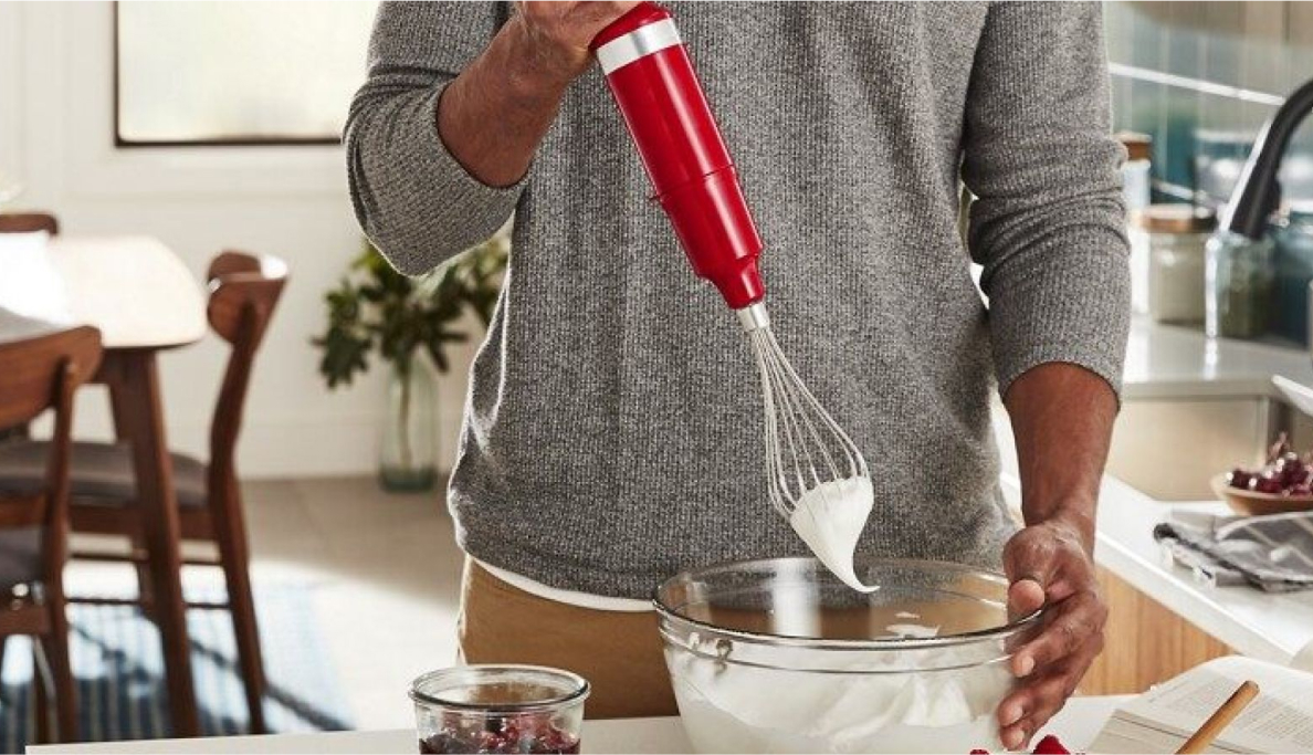 A peson using a hand blender to whip cream.