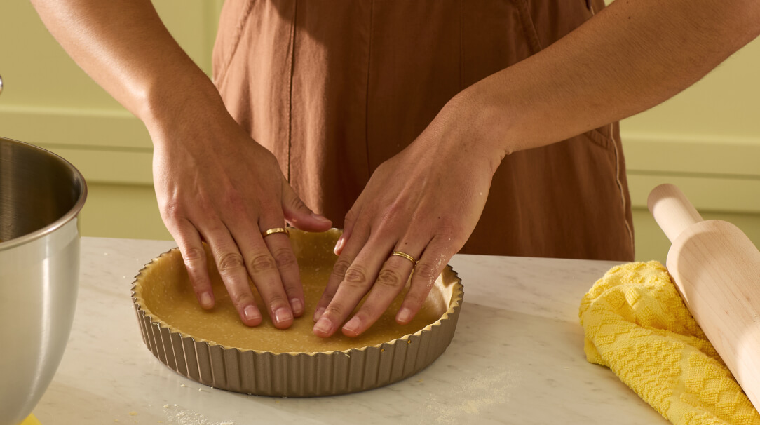 A person pressing a quiche crust into a tart pan.