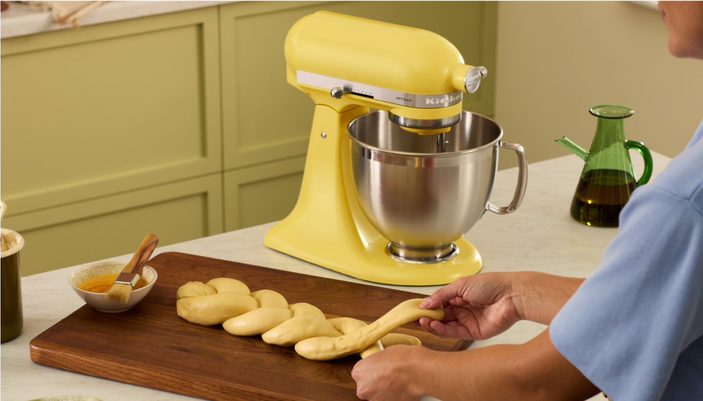 A person braiding dough on a wooden cutting board in front of a Butter KitchenAid Stand Mixer.