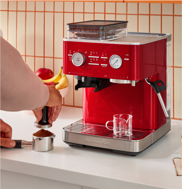 A person tamping down coffee grounds in front of a KitchenAid Espresso Machine
