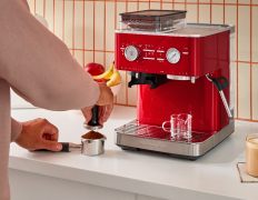 A person tamping down coffee grounds in front of a KitchenAid Espresso Machine