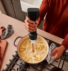 A person using a KitchenAid Go™ Cordless Hand Blender in a dutch oven of soup