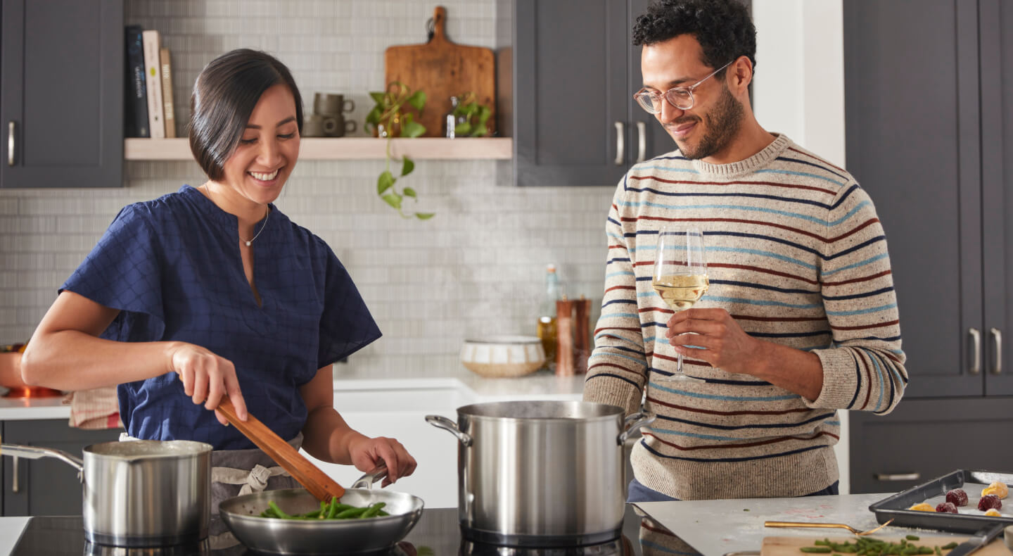 Two people cooking together using several stainless steel pans on an induction cooktop Two people cooking together using several stainless steel pans on an induction cooktop